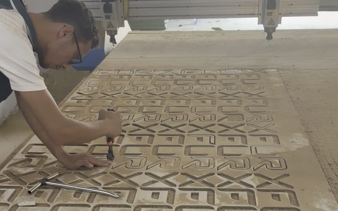 A sheet cut on the CNC router: nested FURX letterforms on the bed, with the router gantry behind and a worker clearing the cut pieces.