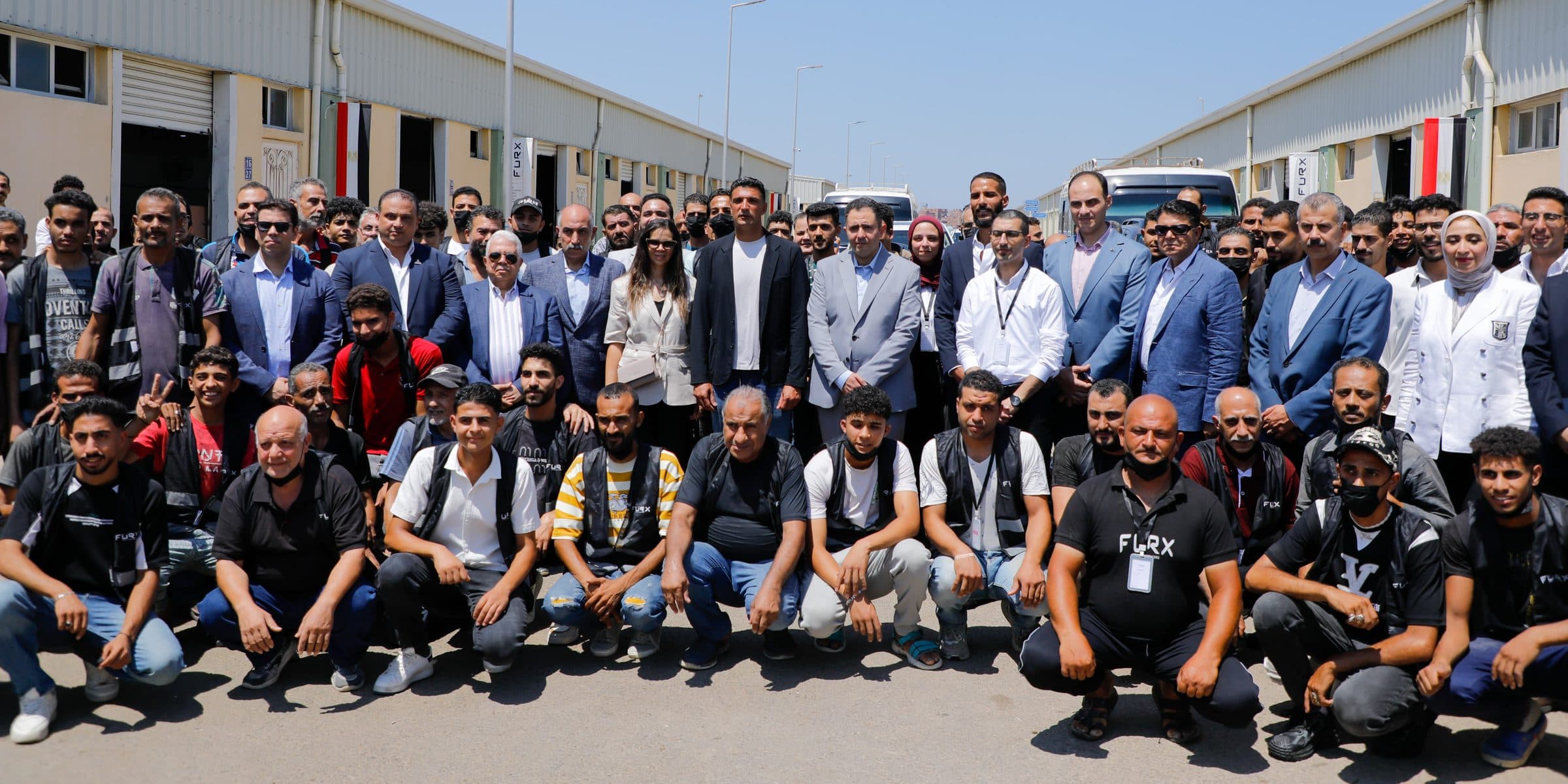 Large group photo of FURX workers with Minister Khaled Hashem and Governor Hossam El-Din Fawzy at centre, between industrial units.