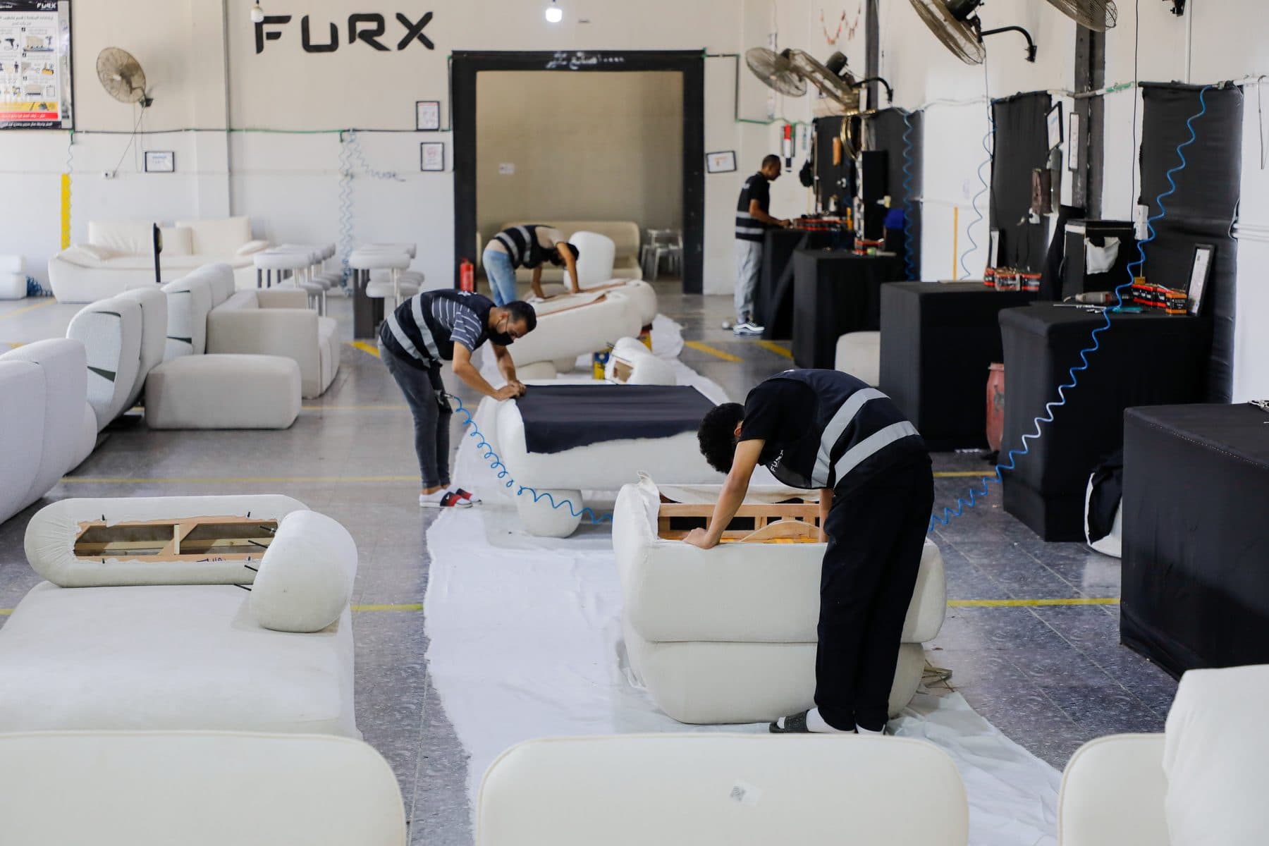 Upholsterers fit covers and dust-cover cloth on sofa bodies laid along a protected work runner.