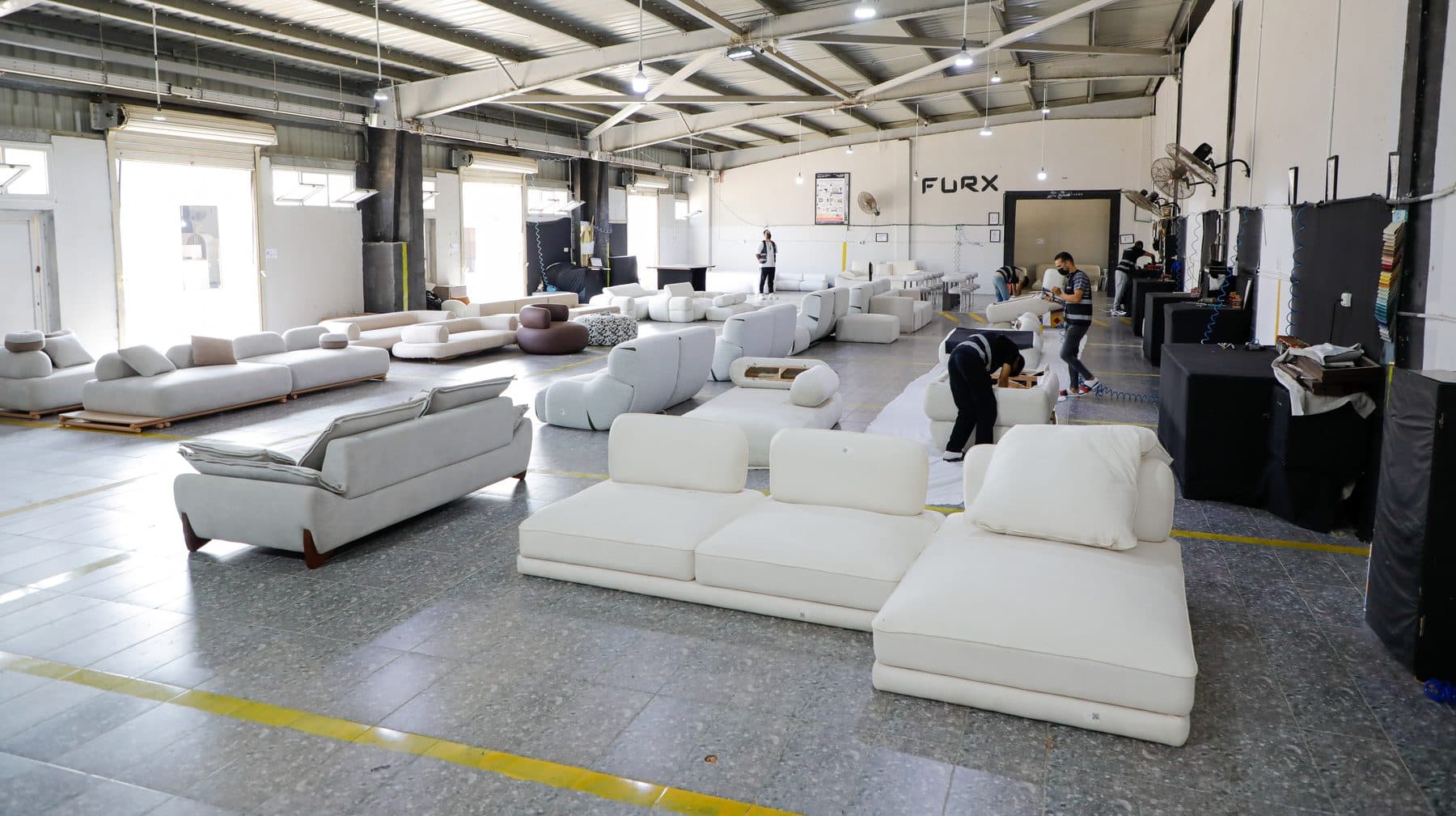 The upholstery finishing hall: finished bouclé sofas staged beside equipped finishing stations.