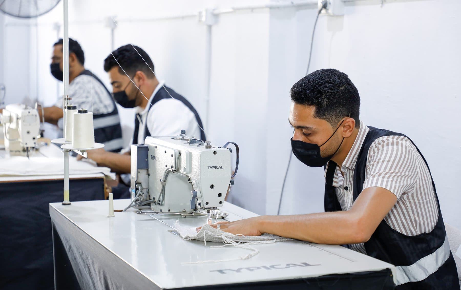 A row of sewing operators stitching textured upholstery fabric on industrial machines.