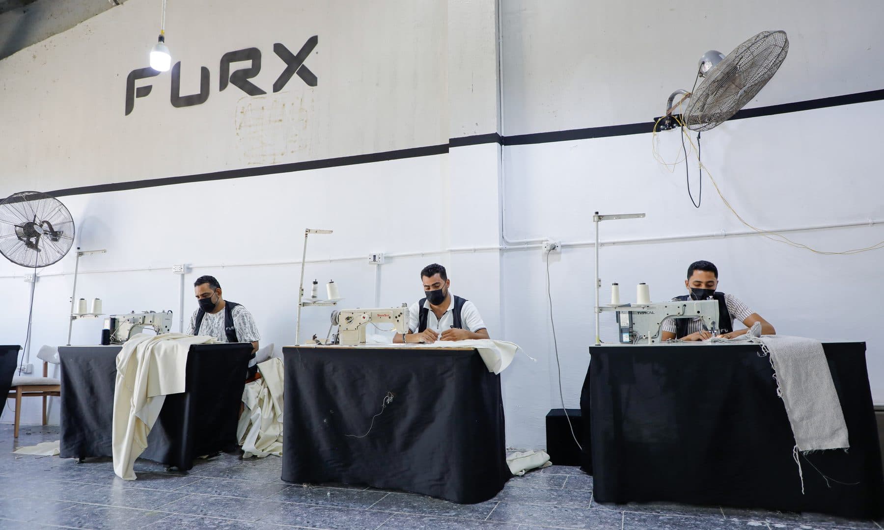 Three masked operators stitch upholstery covers on industrial sewing machines under the FURX wall mark.
