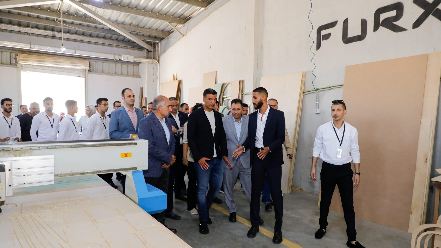Waleed El-Banna gestures as he walks Minister Khaled Hashem and Governor Hossam El-Din Fawzy past a CNC router under the FURX logo.